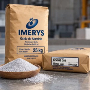Dos sacos de papel kraft de 25 kg de óxido de aluminio Imerys, uno vertical con logotipo azul y otro horizontal con etiqueta BEK95B 080, junto a un recipiente de abrasivo granulado.
